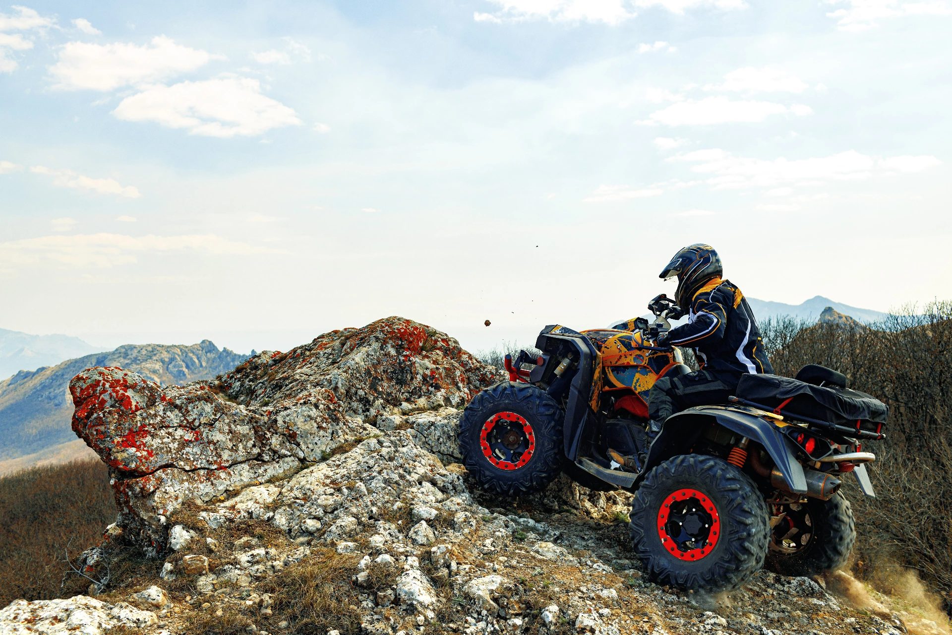 Rider in helmet driving ATV up rocky mountain trail